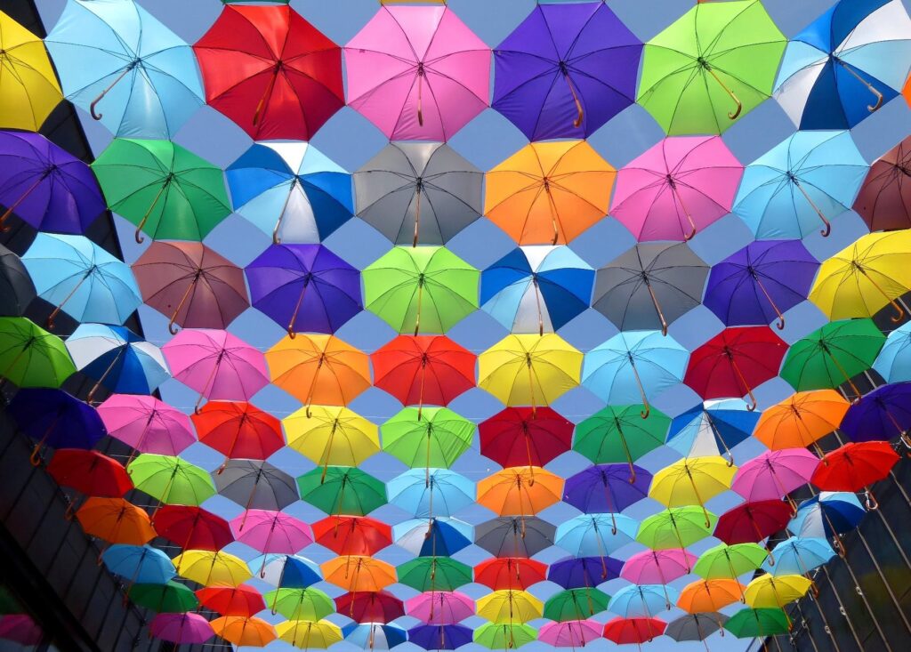 yellow blue red pink purple green multicolored open umbrellas hanging on strings under blue sky